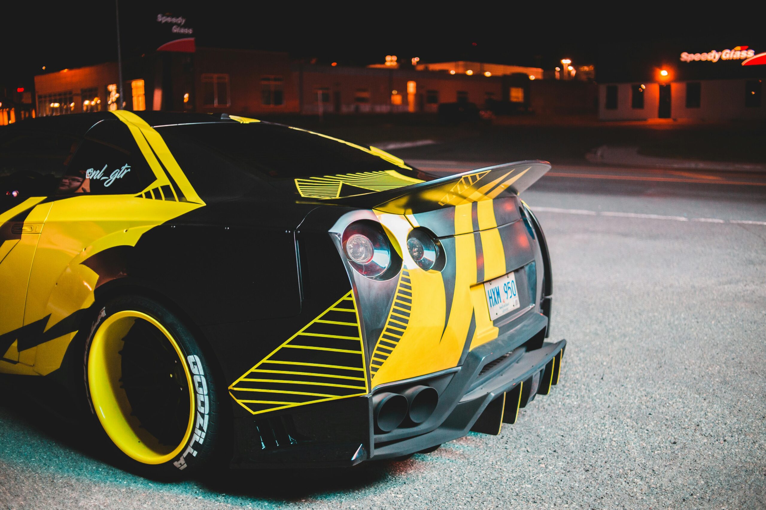 Contemporary sport car with yellow design with back lights parked on asphalt with building in distance in city street at night time
